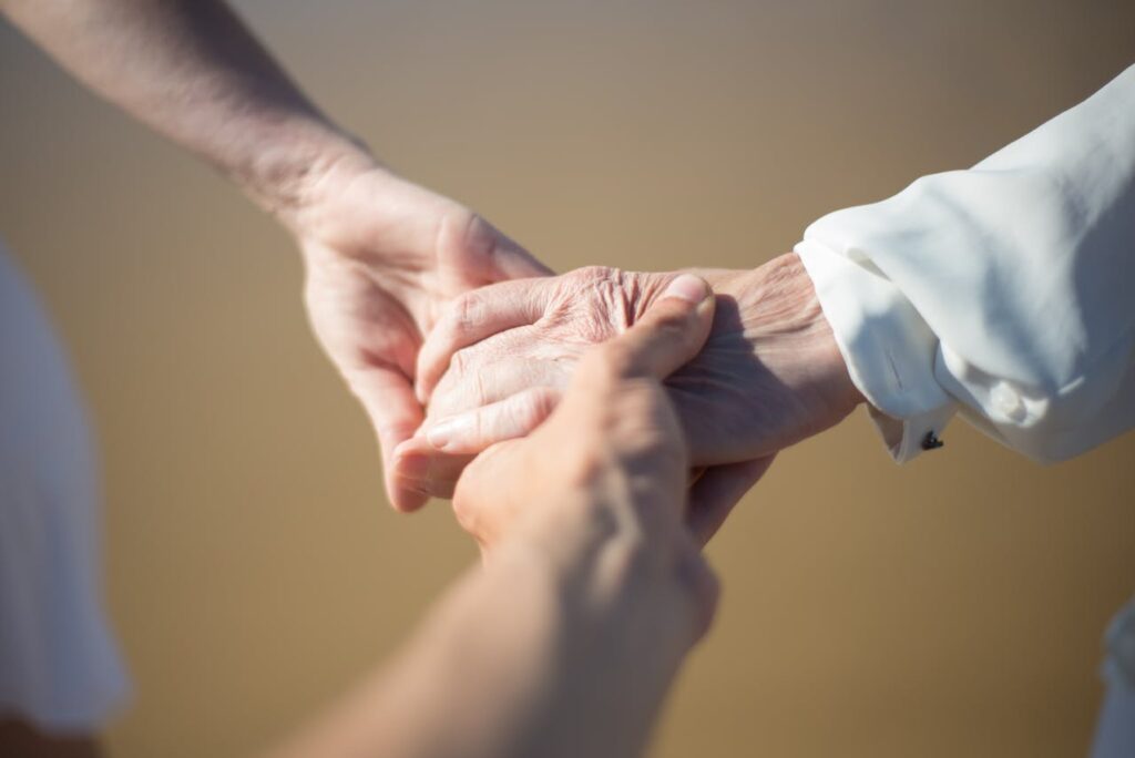 Zwei Menschen halten die Hand einer alten Frau. man sieht nur die drei Hände.